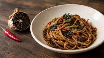Piatto di spaghetti all'aglio nero, olio e peperoncino con lamelle di aglio nero e prezzemolo